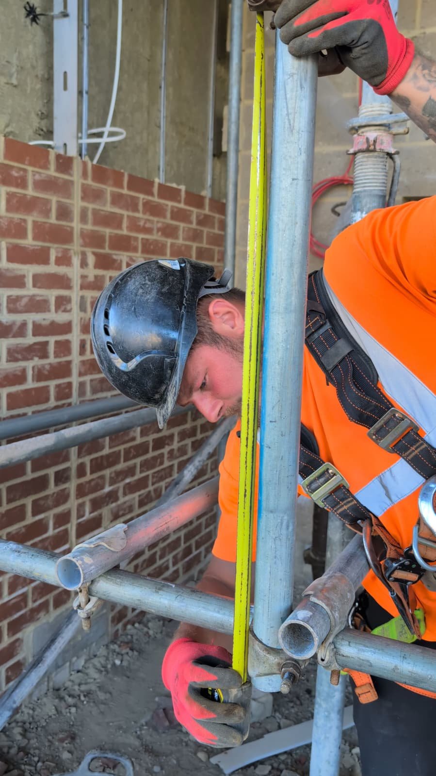 HTK scaffolder in hard hat and harness checking a scaffold joint with a spirit level